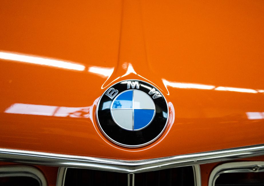 Close-up of a bright orange vintage BMW car hood with emblem, ideal for automotive enthusiasts and classic car lovers.