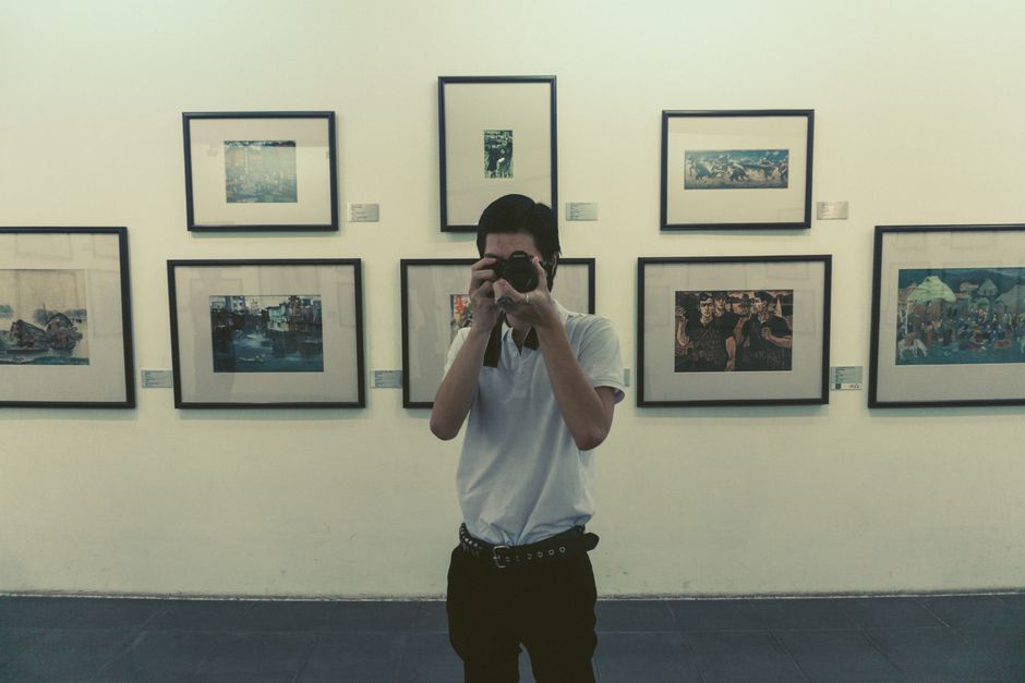 A photographer in a white shirt captures moments in an art gallery filled with framed pictures.