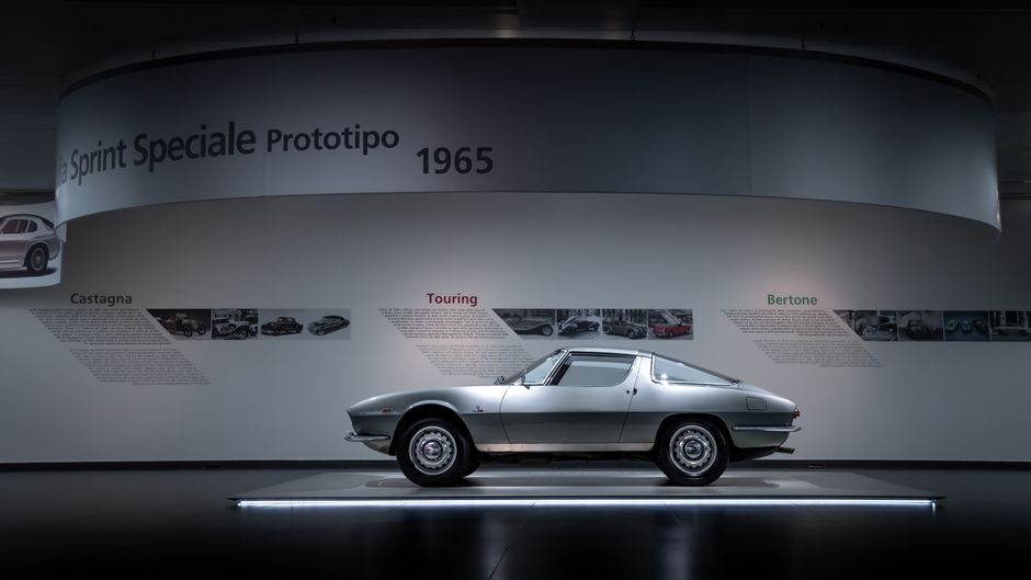 Side view of a 1965 classic car prototype on display in a museum setting.